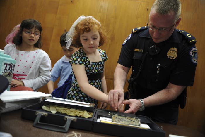 A police officer presses a young girl&#x27;s fingerprints into an ink pad