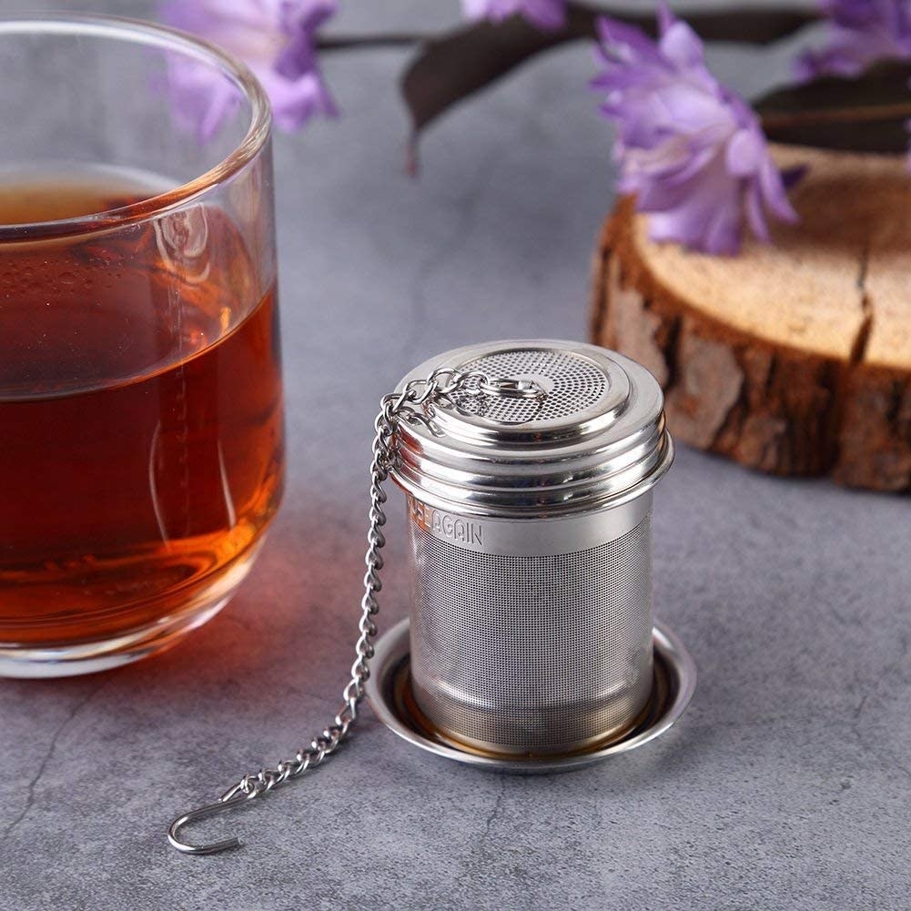 The infuser on a thin metal plate next to a glass of tea