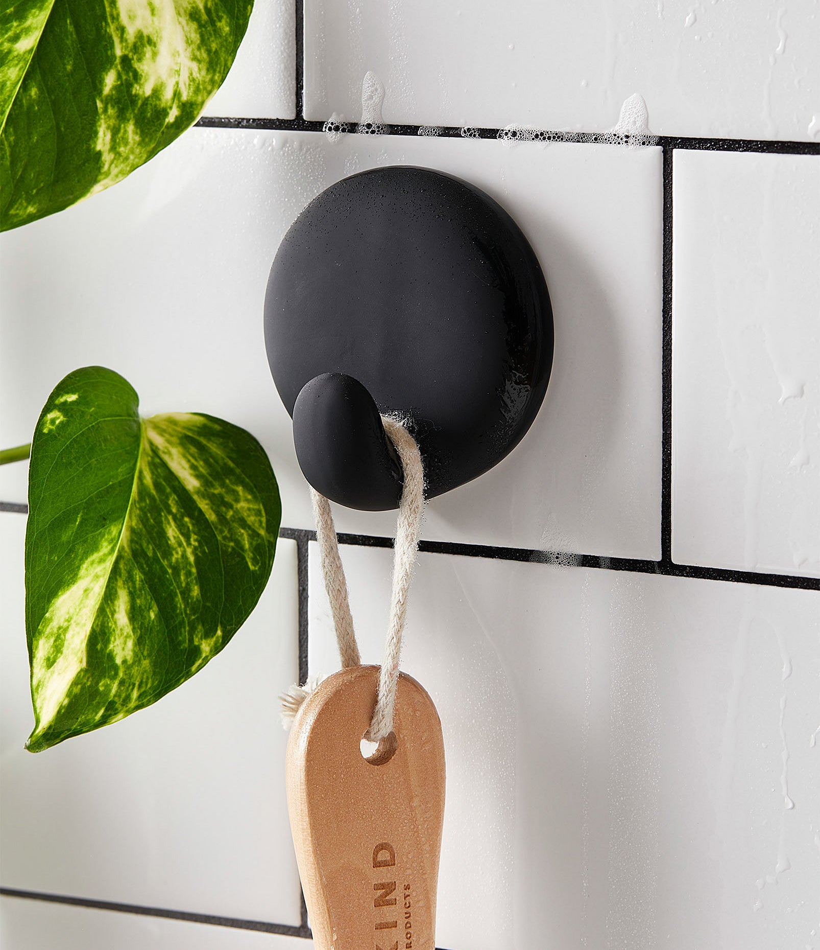 A small hook attached to a tiled wall with a wooden brush hanging from it