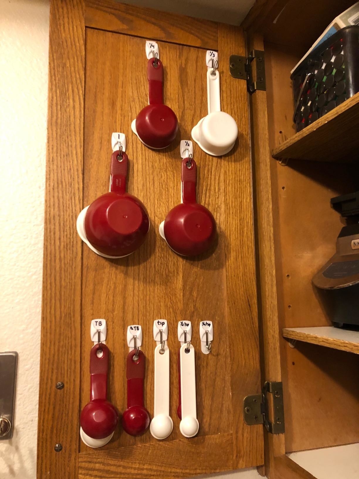 reviewer photo showing the command strips used to hang measuring cups on back of cupboard 