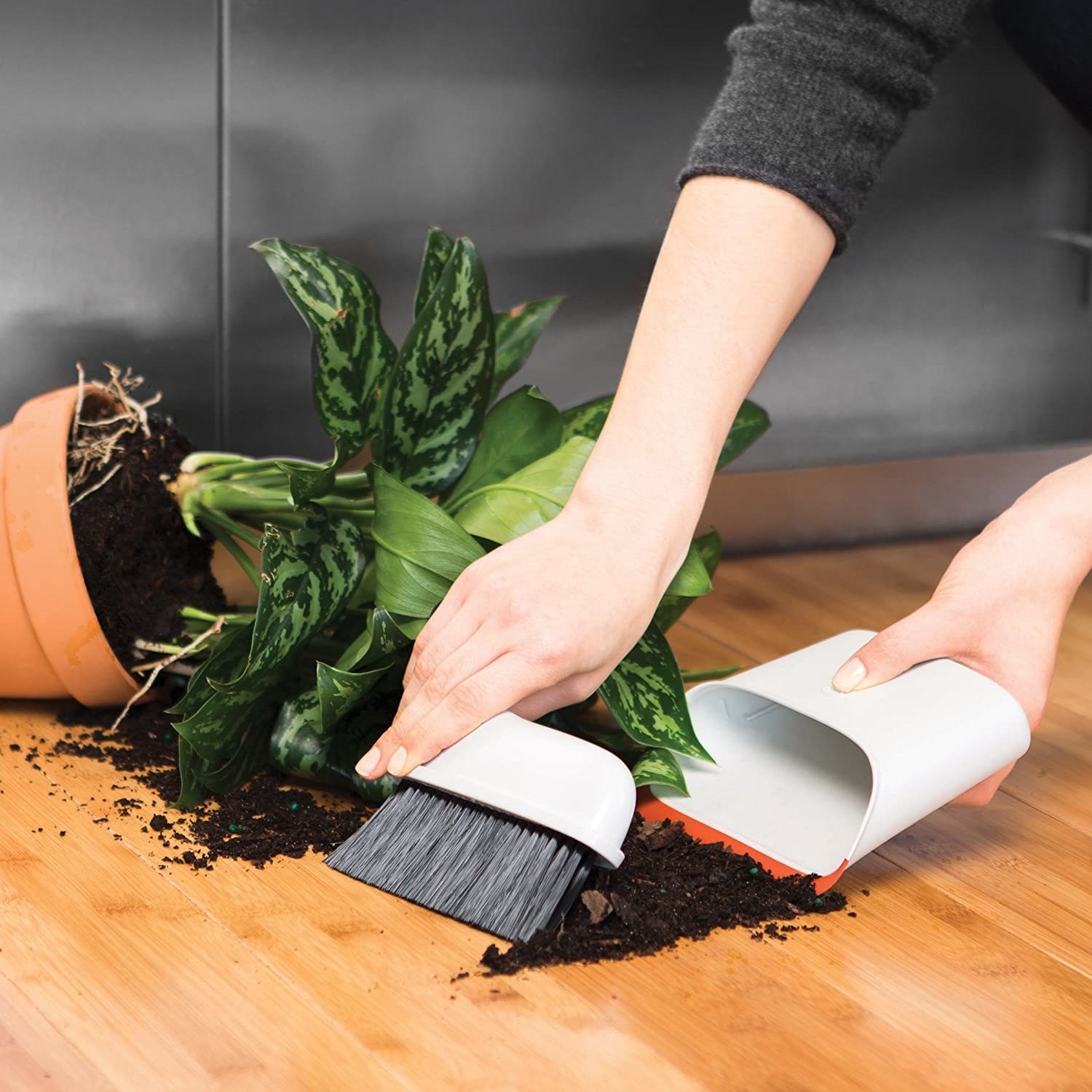 Someone sweeping up spilled dirt with the mini broom and dustpan