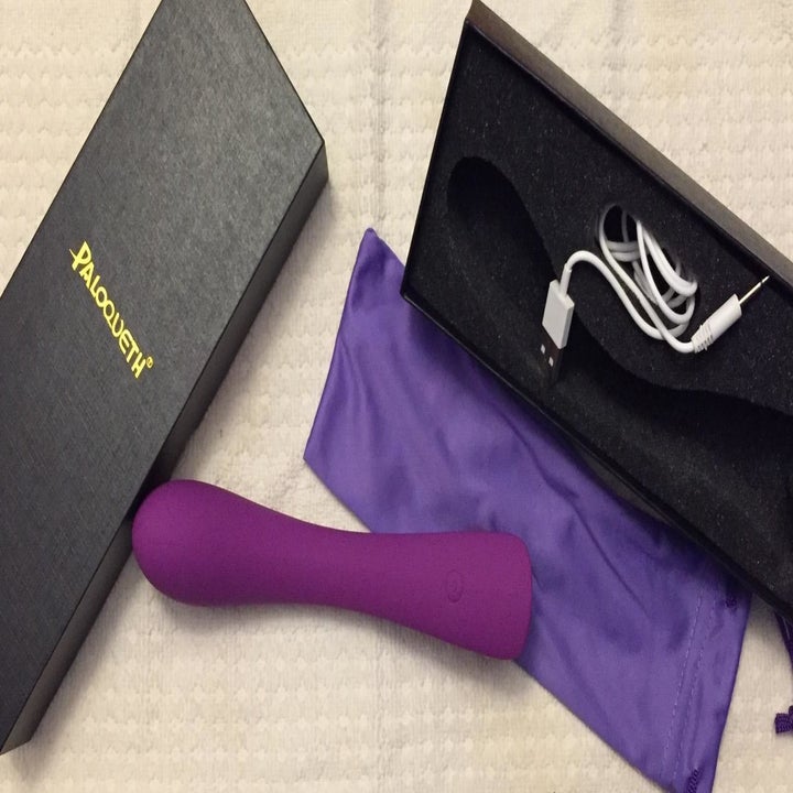 A reviewer photo of the purple, vibrating dildo with the USB charging cord, gift box, and matching storage pouch 