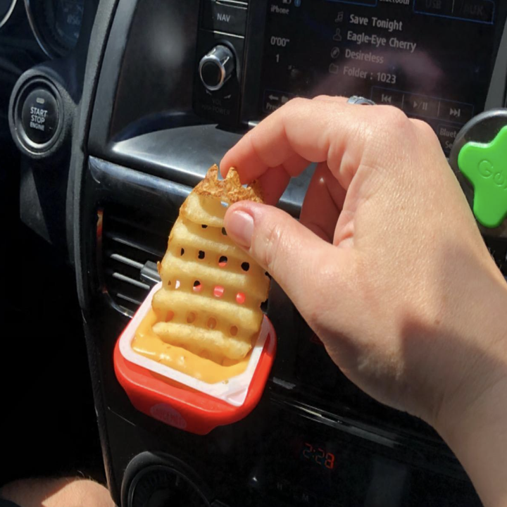 a person dipping a waffle fry into a sauce being held by the car dip clip