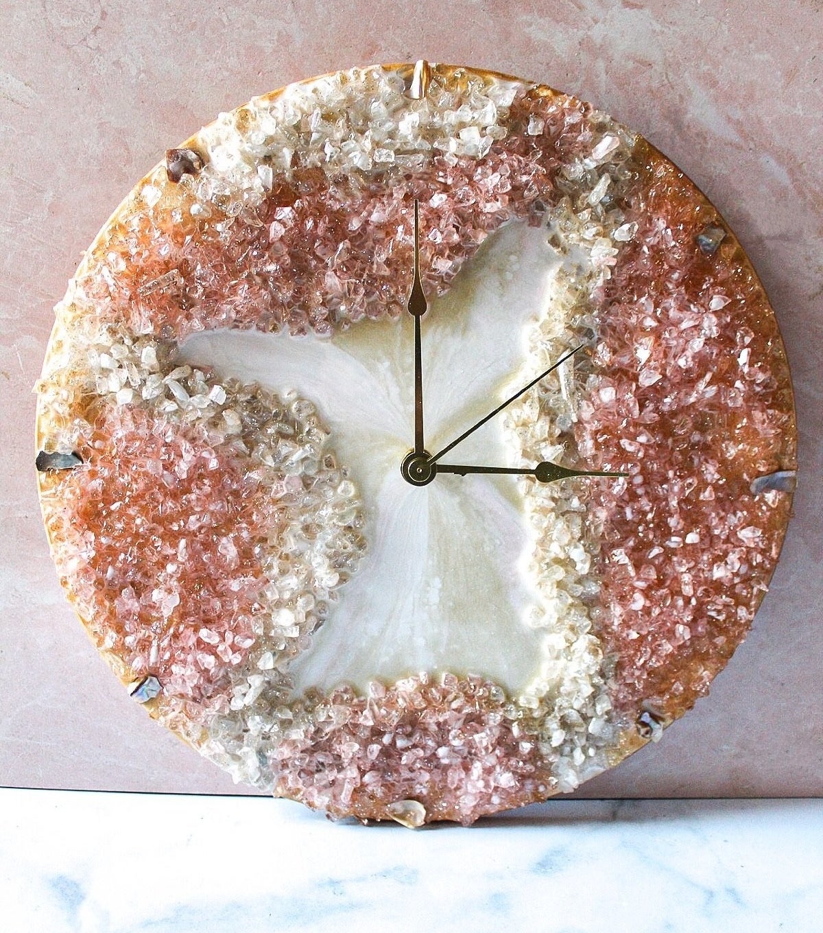 circular clock with pink, orange, and white geodes all over it and gold wire hands