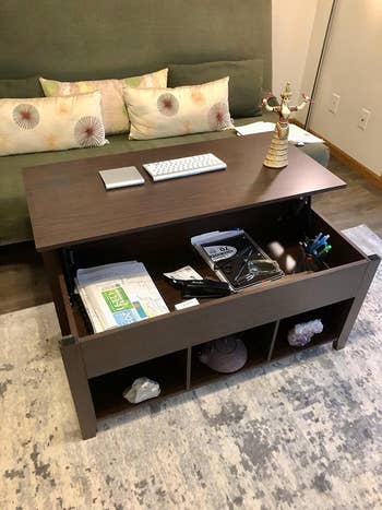 the same reviewer now showing the top of the coffee table lifted forward toward a couch with assorted things stored in the inside