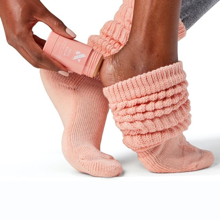 a model applying balm to the back of their heels while wearing pink socks