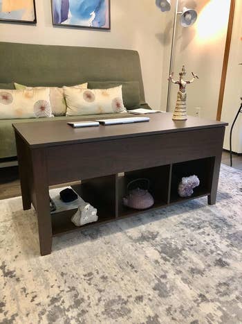 reviewer image of the coffee table in brown with three cubbies for storage across the bottom