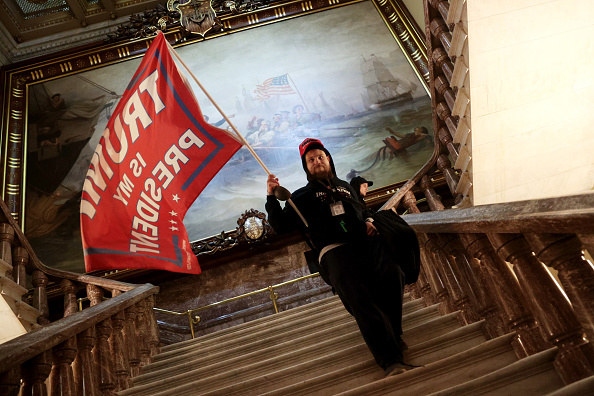 A man walks down steps inside the Capitol holding a Trump flag