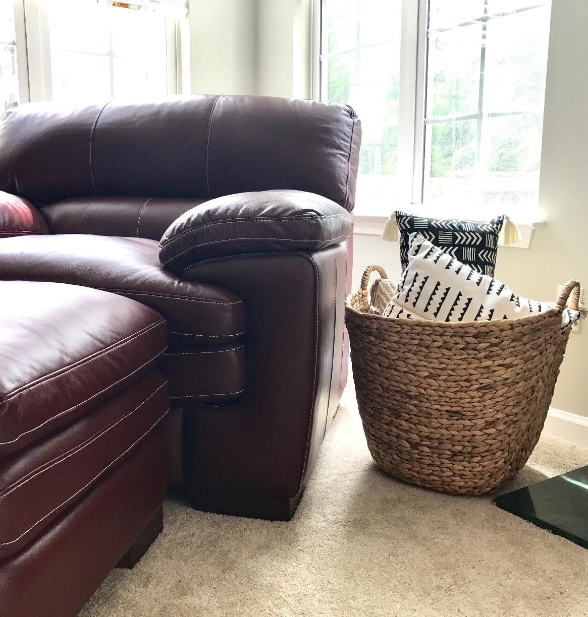 reviewer pic of the woven basket in light tan next to a chair with pillows inside of it