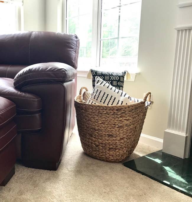 reviewer pic of the woven basket in light tan next to a chair with pillows inside of it