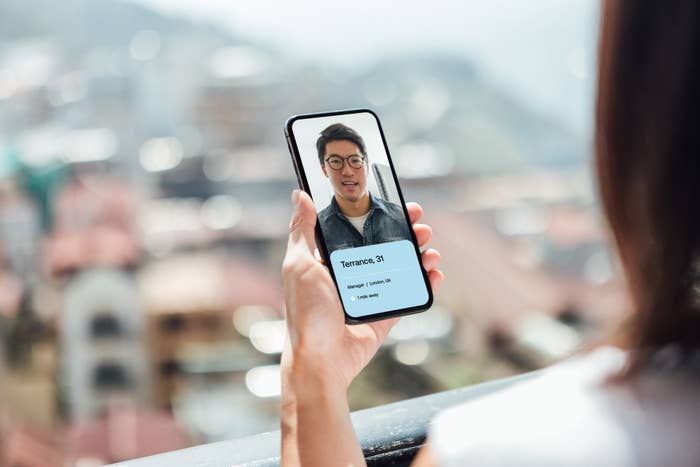 A dating profile on a phone being held up by a woman&#x27;s hand