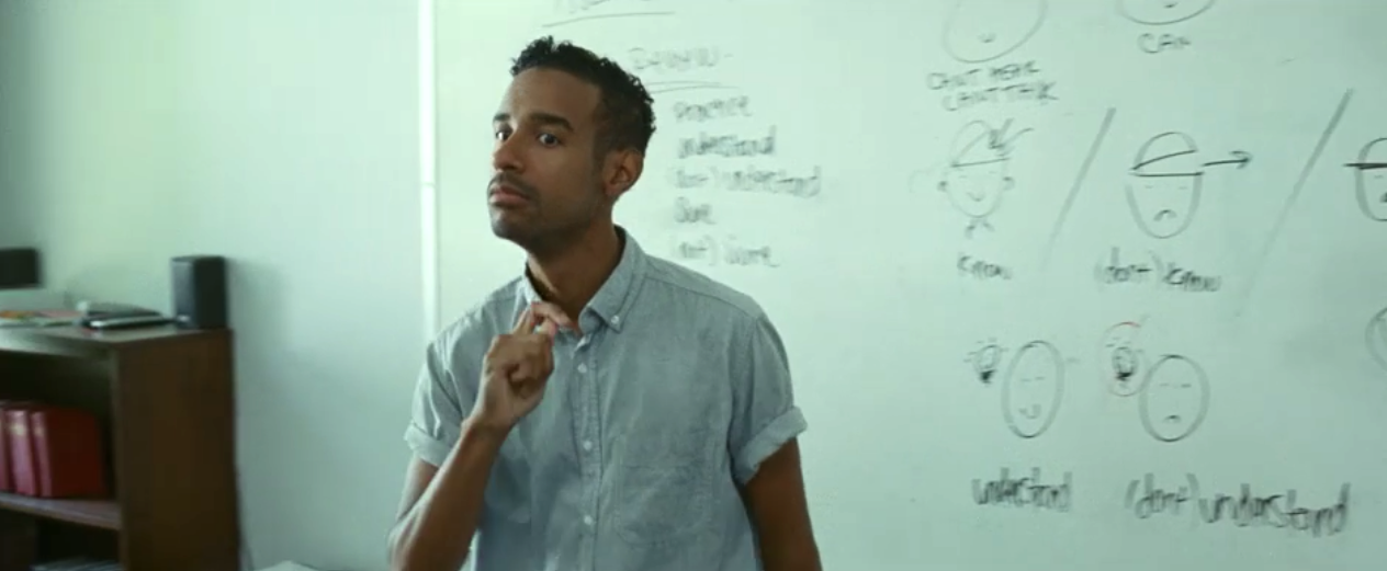 Jeremy Lee Stone as an ASL teacher, signing in front of a white board for a class