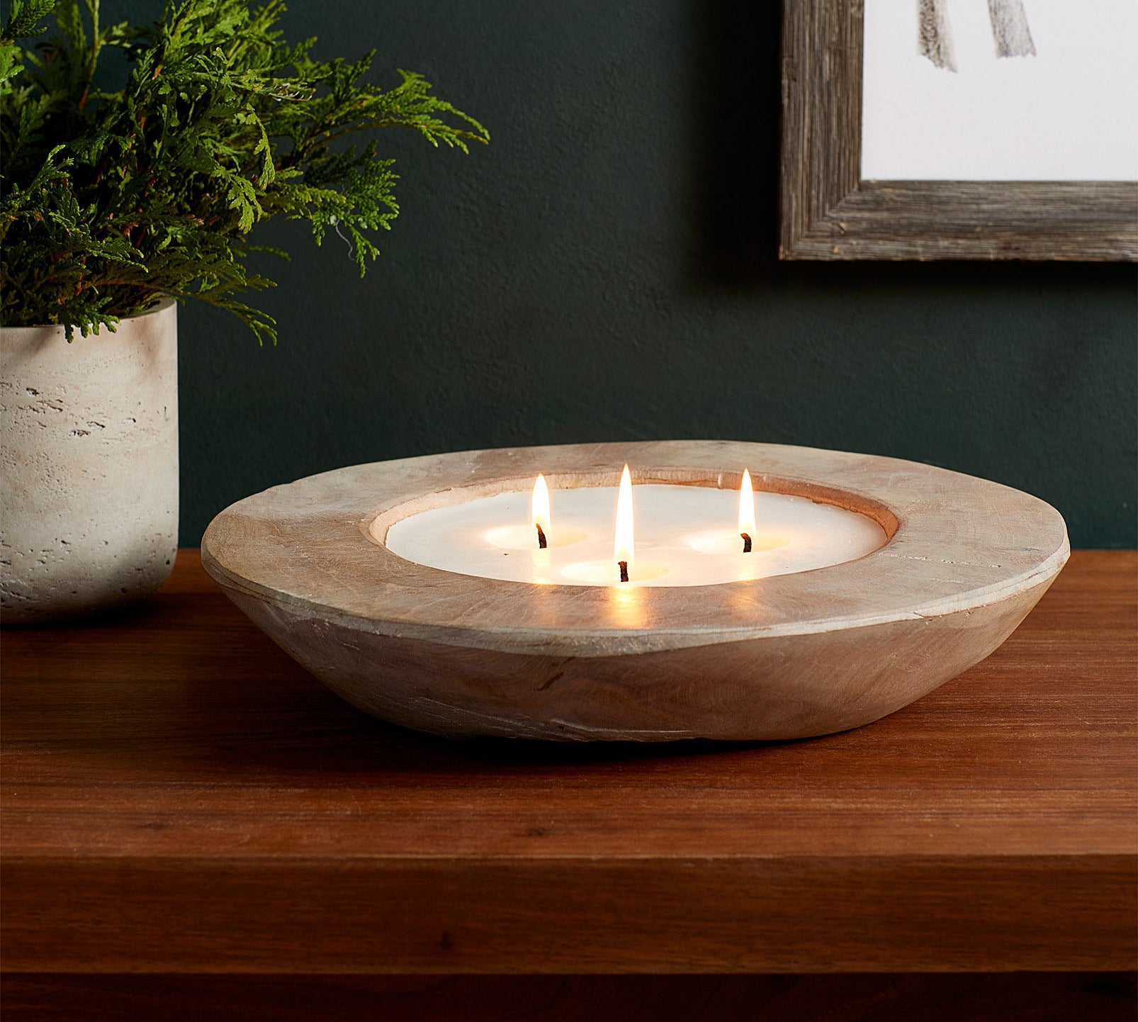 The candle's triple wicks lit on a wooden table next to a plant