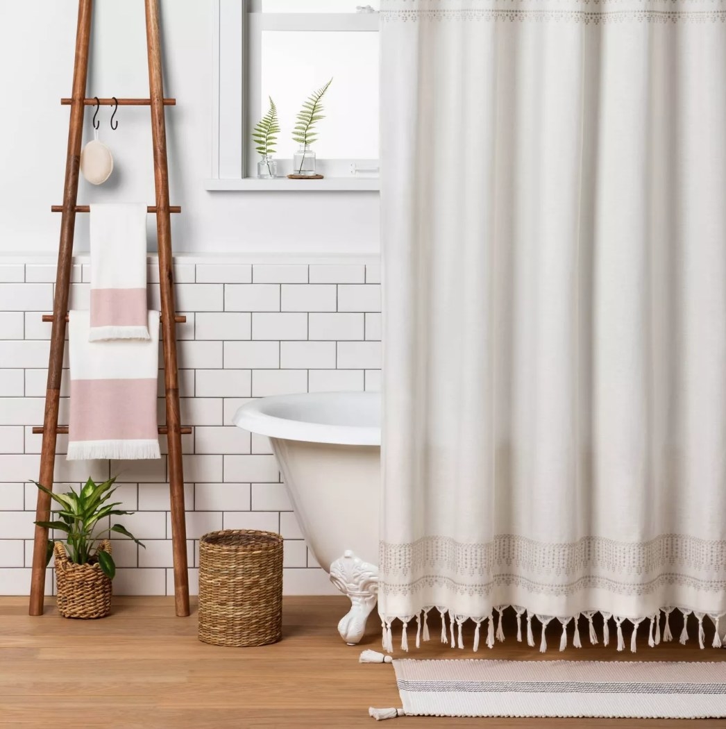 Cream colored shower curtain with tassels in front of white tub 