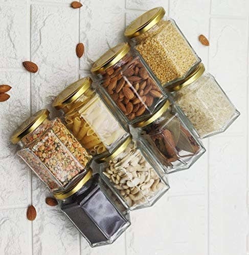 A set of 8 hexagonal jars with golden lids with food items in them