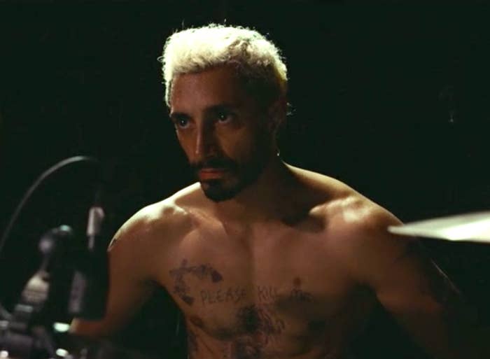 Riz Ahmed as Ruben, shirtless and covered in tattoos, playing drums