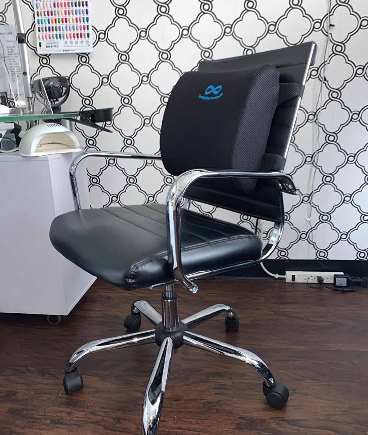 A reviewer photo of a black leather office chair with the lumbar support pillow strapped to the back 