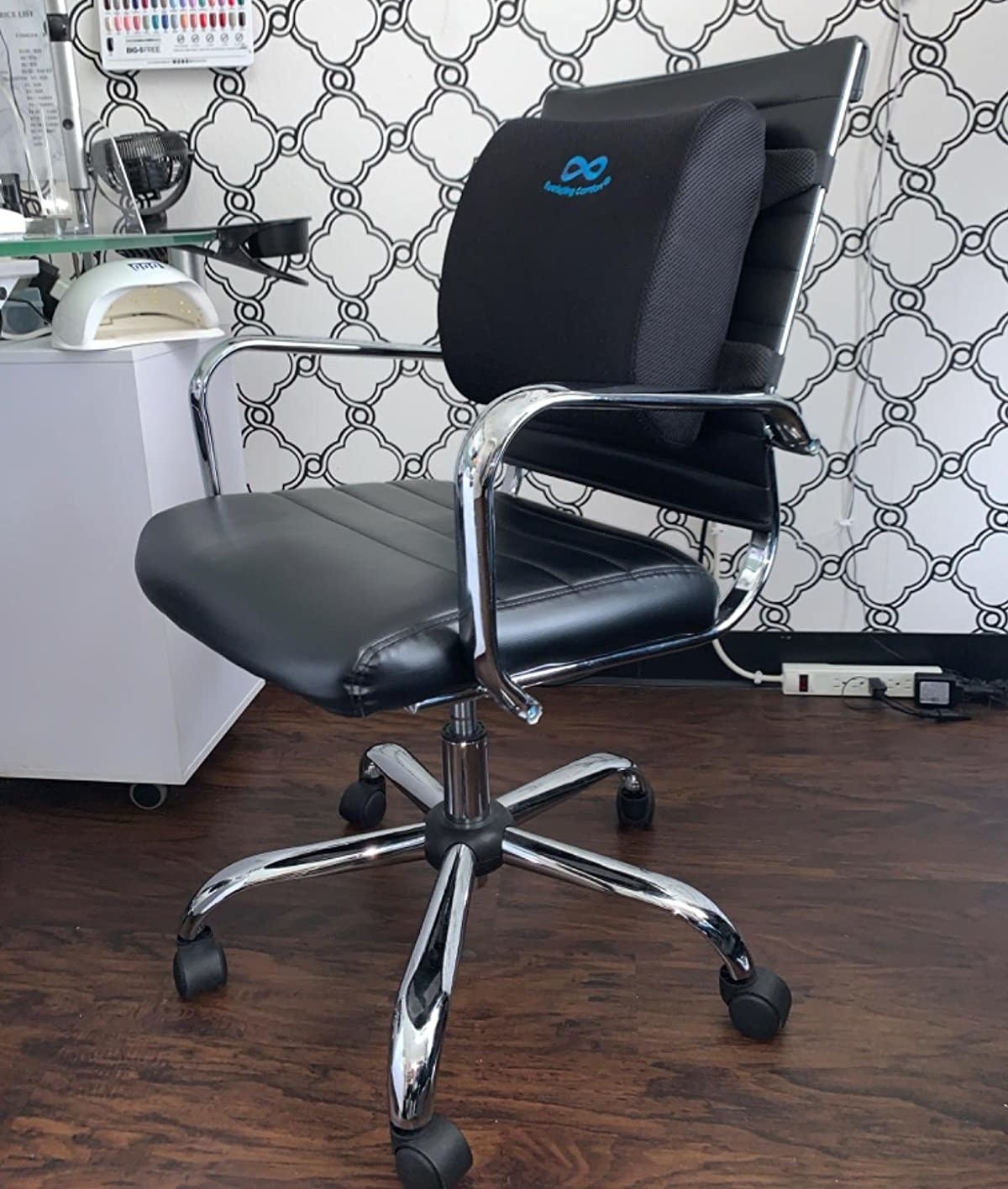 A reviewer photo of a black leather office chair with the lumbar support pillow strapped to the back