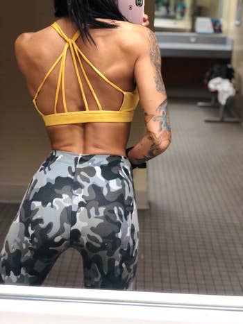 reviewer showing the back of the sports bra with the strappy design in yellow