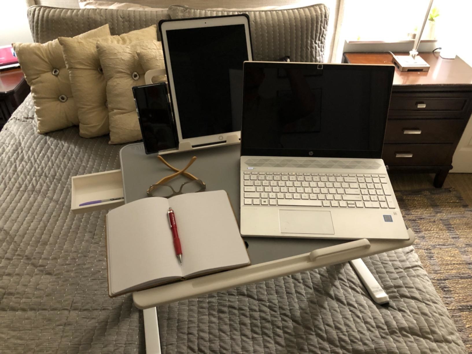 reviewer image of the laptop bed tray with a phone, tablet, laptop, and notebook on its surface