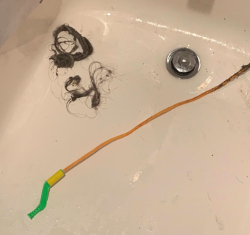 A reviewer photo of a FlexiSnake on the floor of a tub after pulling out a mound of hair