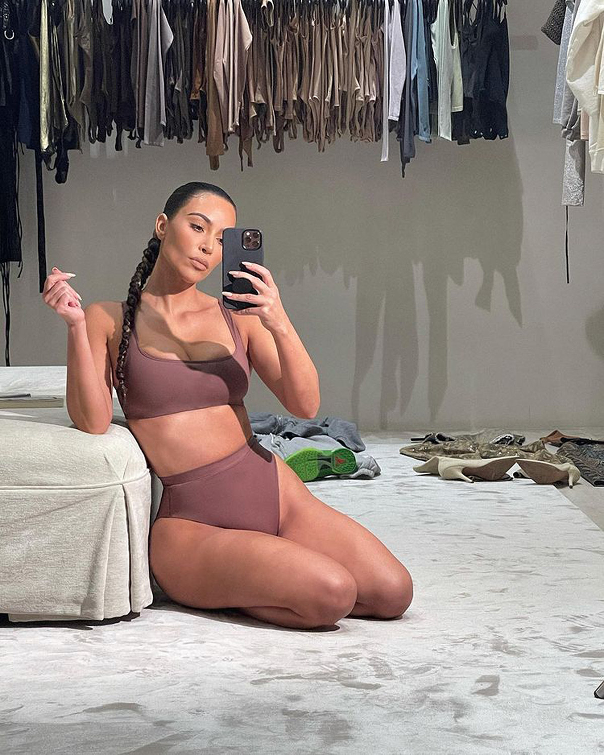 Kim taking a picture of herself wearing shapewear with her hair in a braided ponytail
