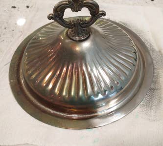 A silver lid with half of it untreated and tarnished then the other half looking like new