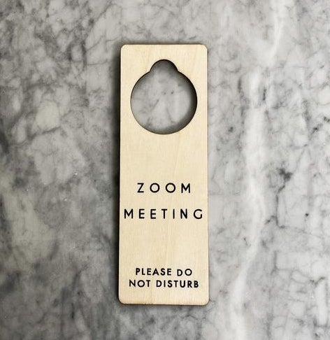 A natural wood doorknob hanging sign that says "Zoom Meeting, please do not disturb" in simple black letters"