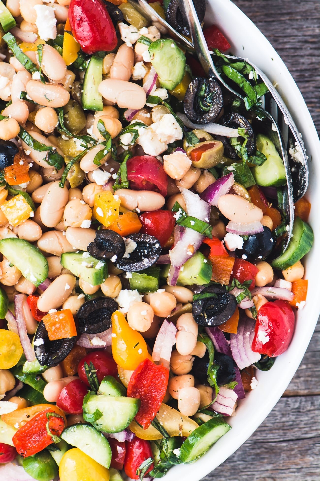 A salad with tomatoes, cucumber, white beans, red onions, and olives.