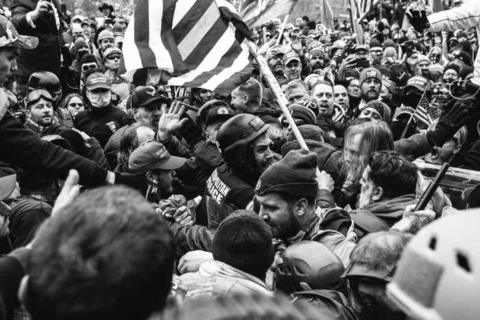 A police officer in riot gear is swamped by dozens of insurrectionists