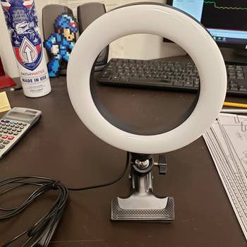 A reviewer photo of an unlit ring light with an attached clamp sitting on a desk 