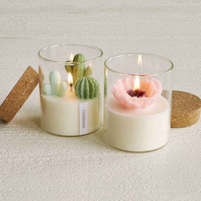 glass candle holder with a cork top and white wax, and either three wax cacti or a wax flower on top 