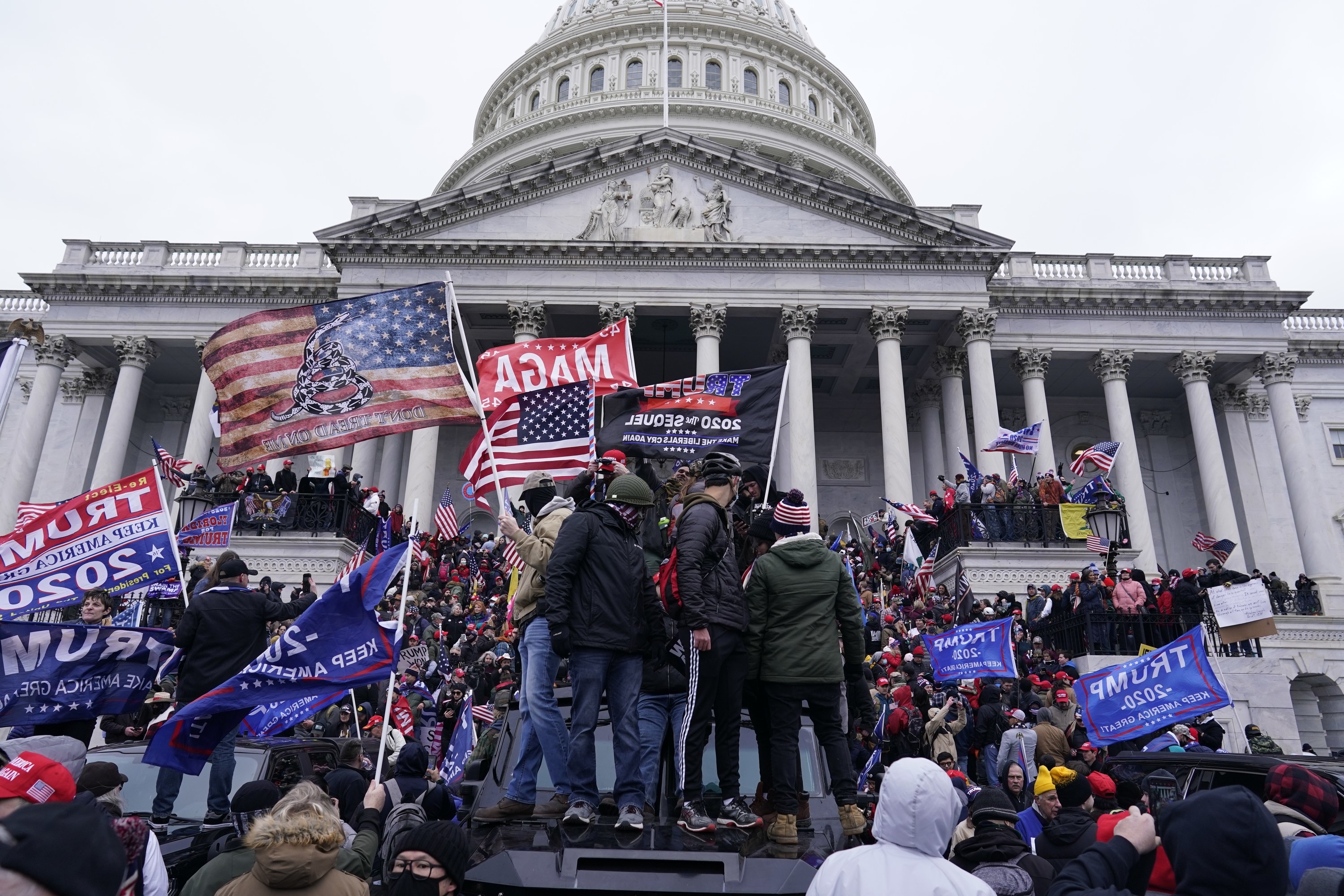 A mob of Trump supporters, waving MAGA and &quot;Trump 2020&quot; flags, stand outside the US Capitol building, some standing on top of an armored car