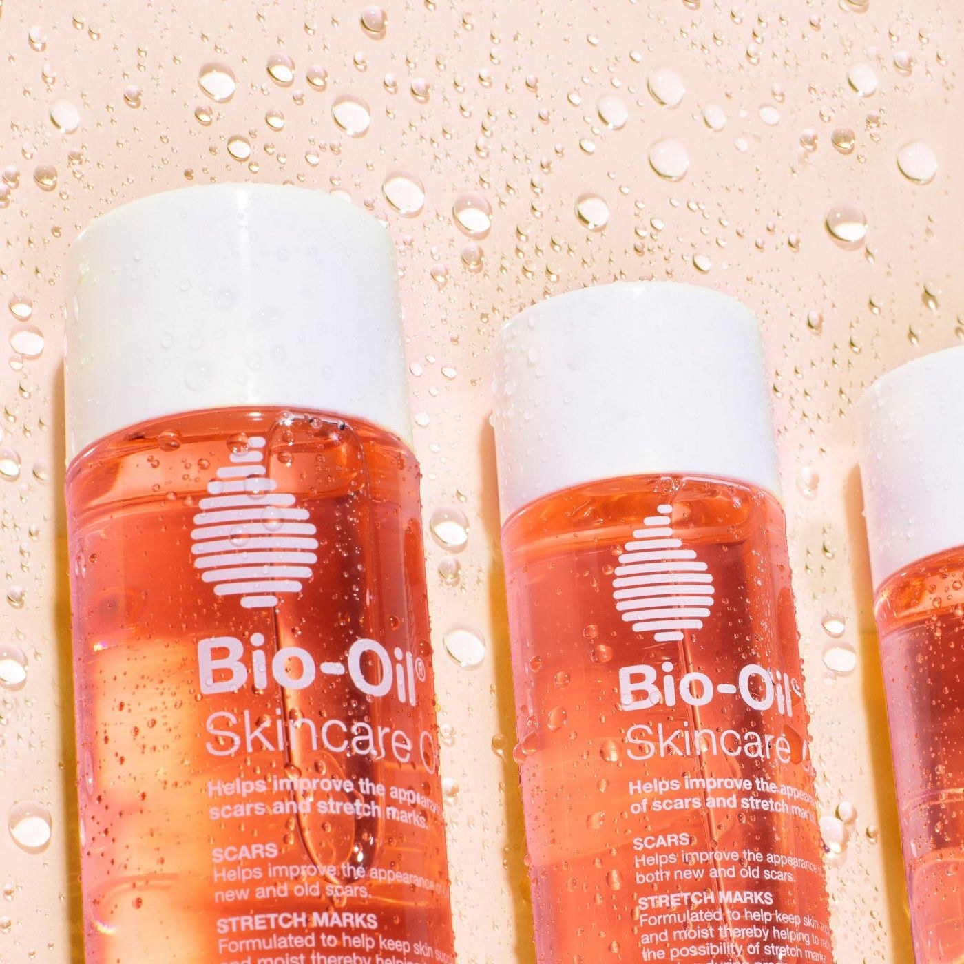 three bottles of orange bio-oil on a wet surface
