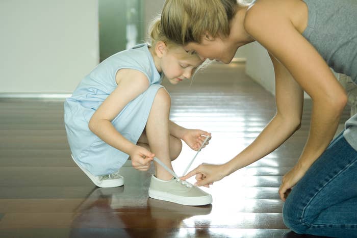 A woman helping a child tie her shoe
