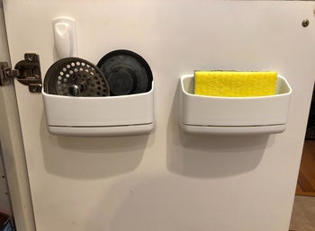 Two of the caddy's on the inside of a reviewer's cabinet door, holding drain plugs and a sponge