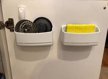 Two of the caddy's on the inside of a reviewer's cabinet door, holding drain plugs and a sponge