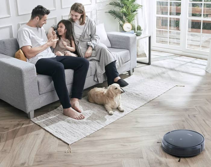 People on a couch next to a robot vacuum on the floor