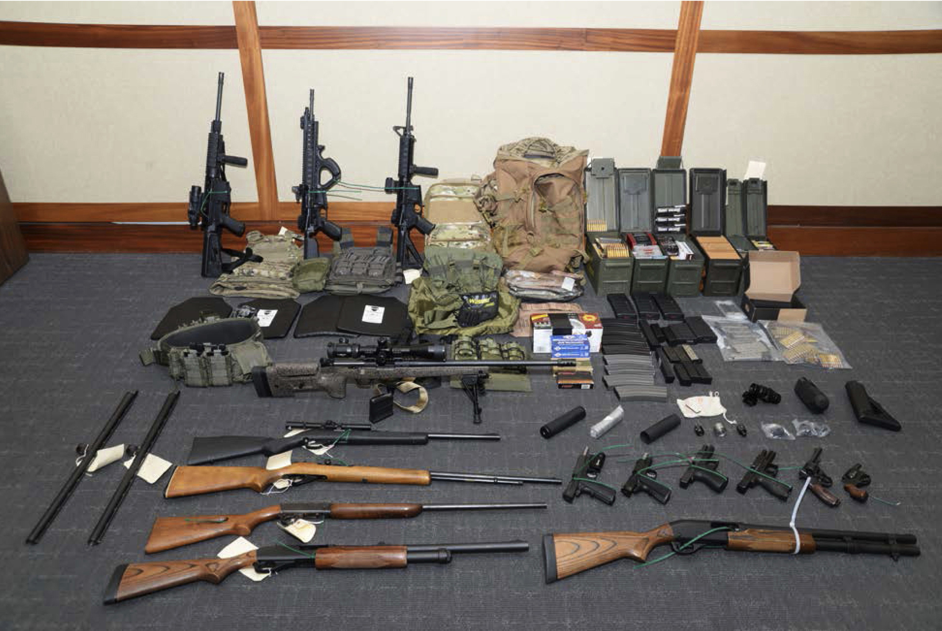 A collection of ammunition and various guns are displayed on the ground against a wall