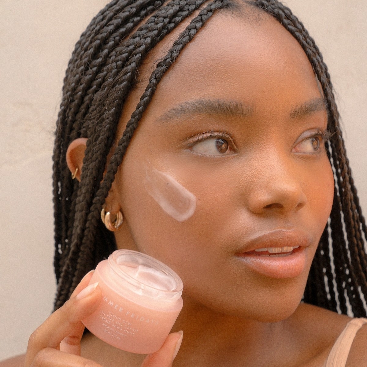model holding the circular short container in light pink with a schmear of moisturizer on their face