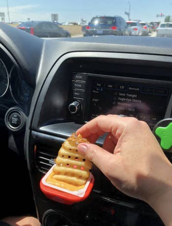 reviewer dipping fry into sauce that's placed in the dip clip and attached to car vent