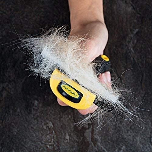A person holding up the deshedding tool with loose fur on it