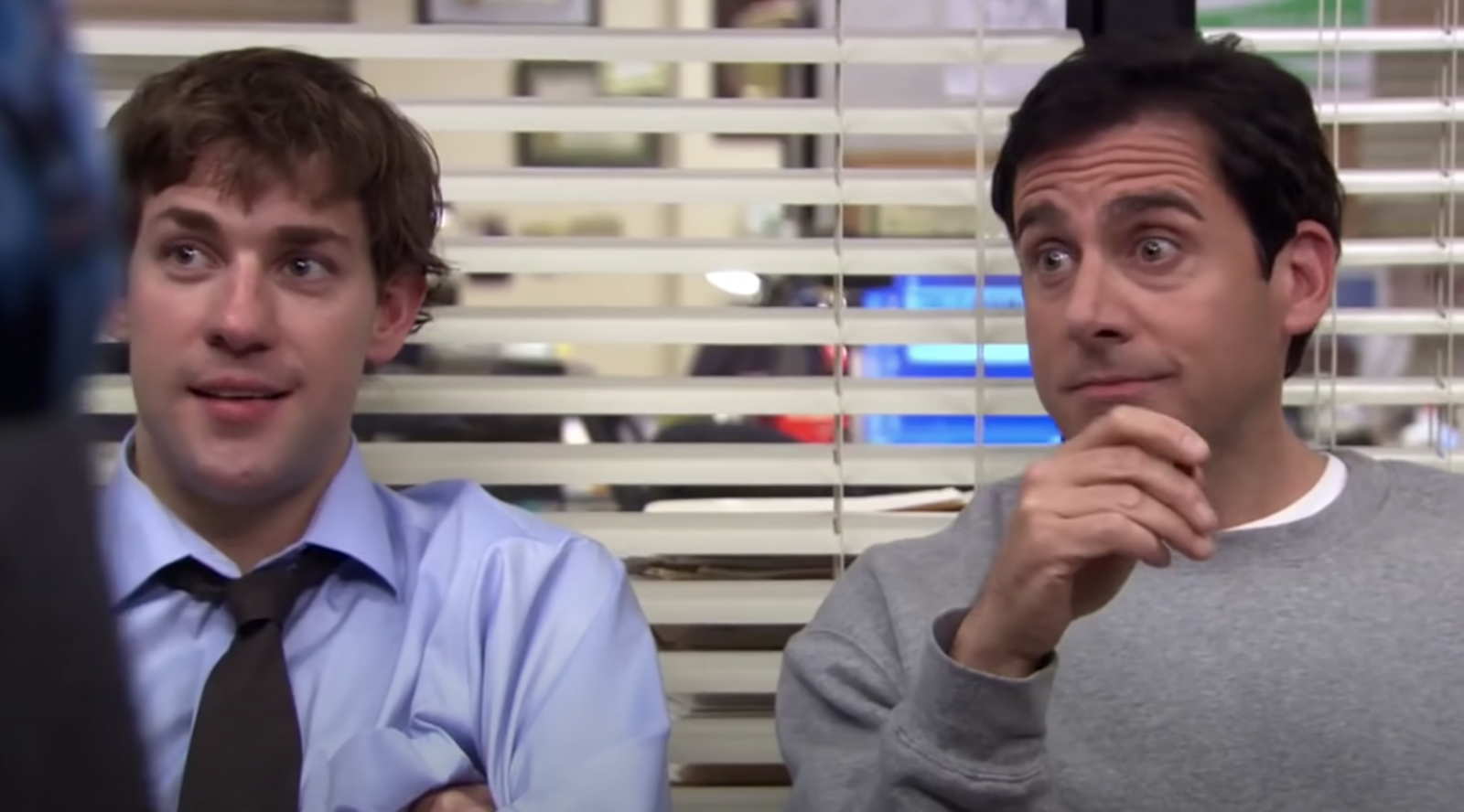 two men, one in a button down and tie, the other in a crewneck sweatshirt, sit in an office conference room, smiliing