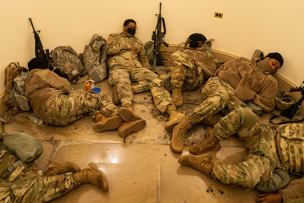 National Guard members rest on the floor with their weapons next to them in the Capitol
