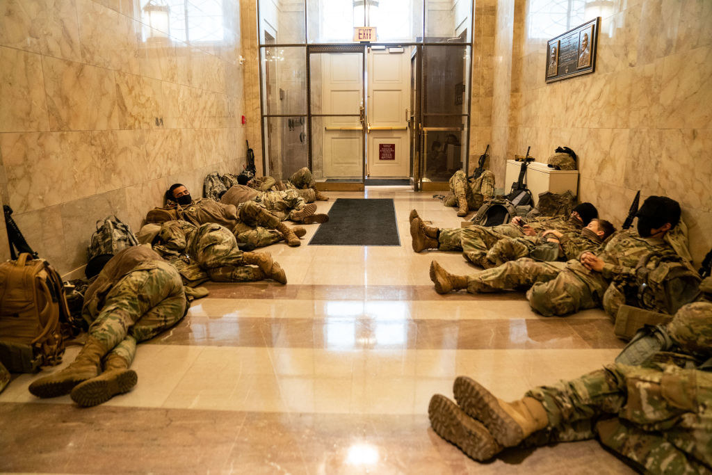 National Guard members rest on the floor with their weapons next to them in the Capitol