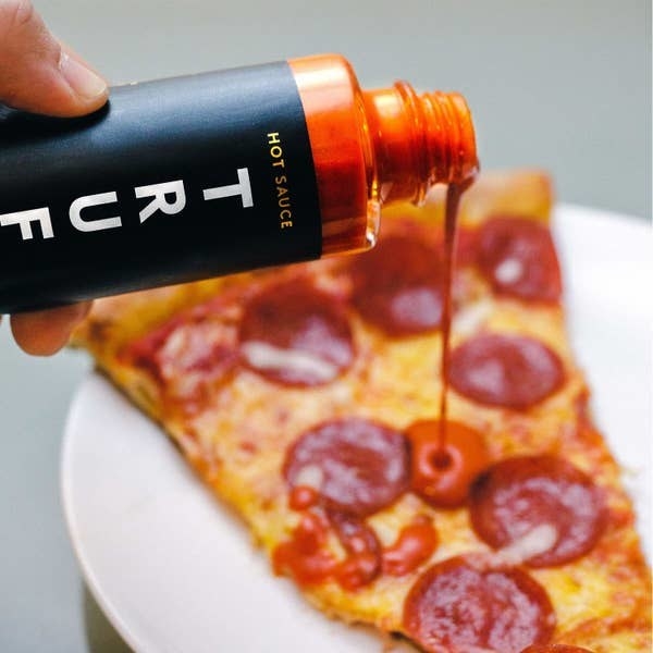 a person pouring the truffle hot sauce on a slice of pepperoni pizza