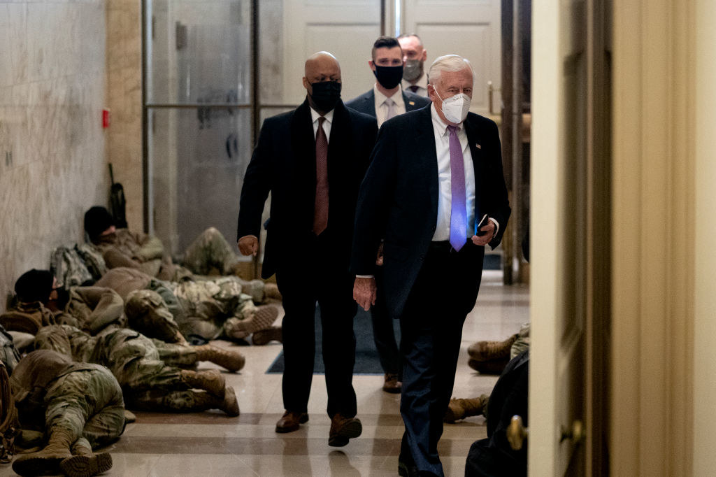 Officials walk by National Guard members as they rest on the floor