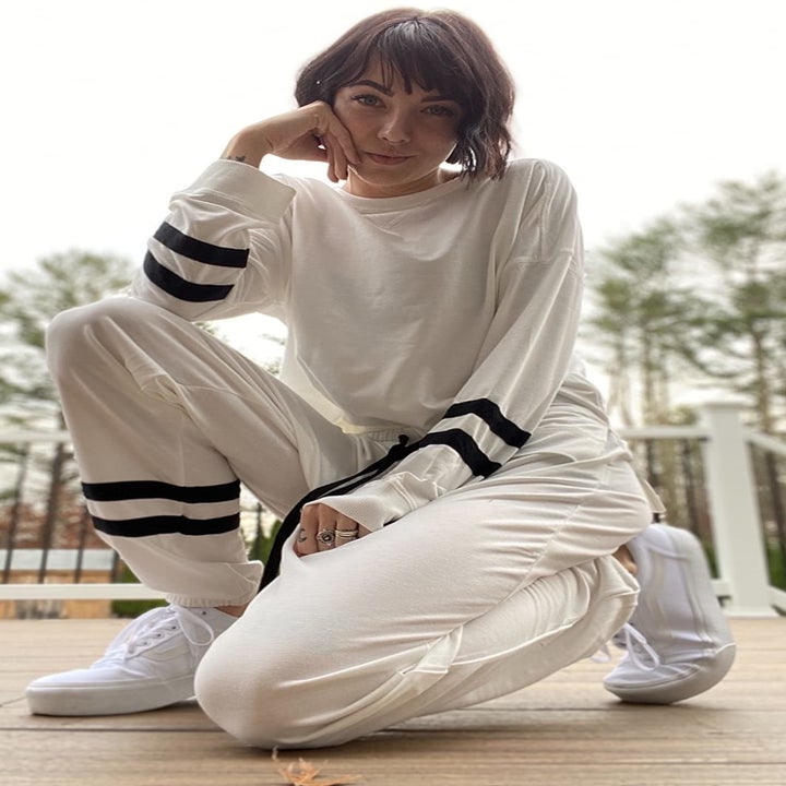 A reviewer wearing the white sweatshirt and pants with black athletic stripes