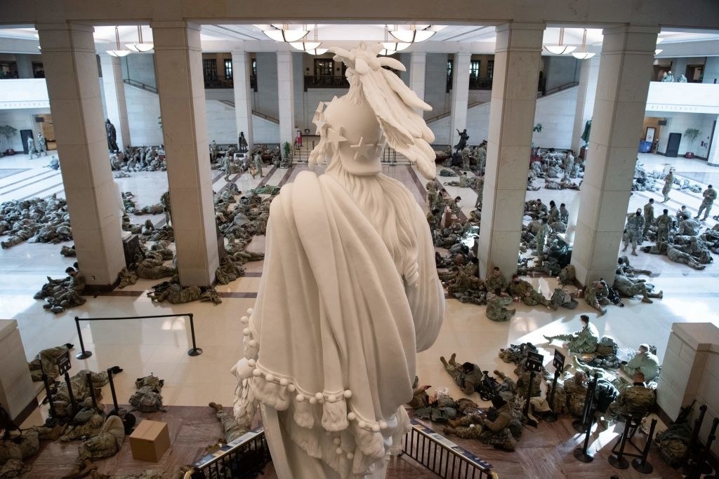 Armed National Guard members sitting and sleeping on the floor in front of a statue inside the Capitol