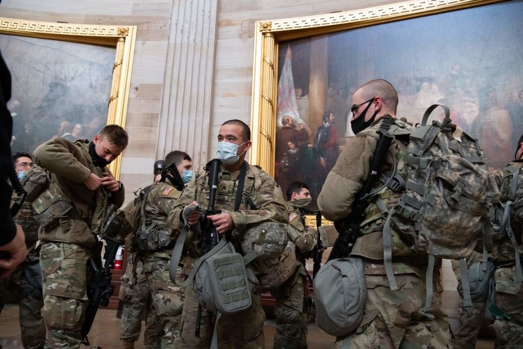 Several members stand in front of paintings inside the Capitol 